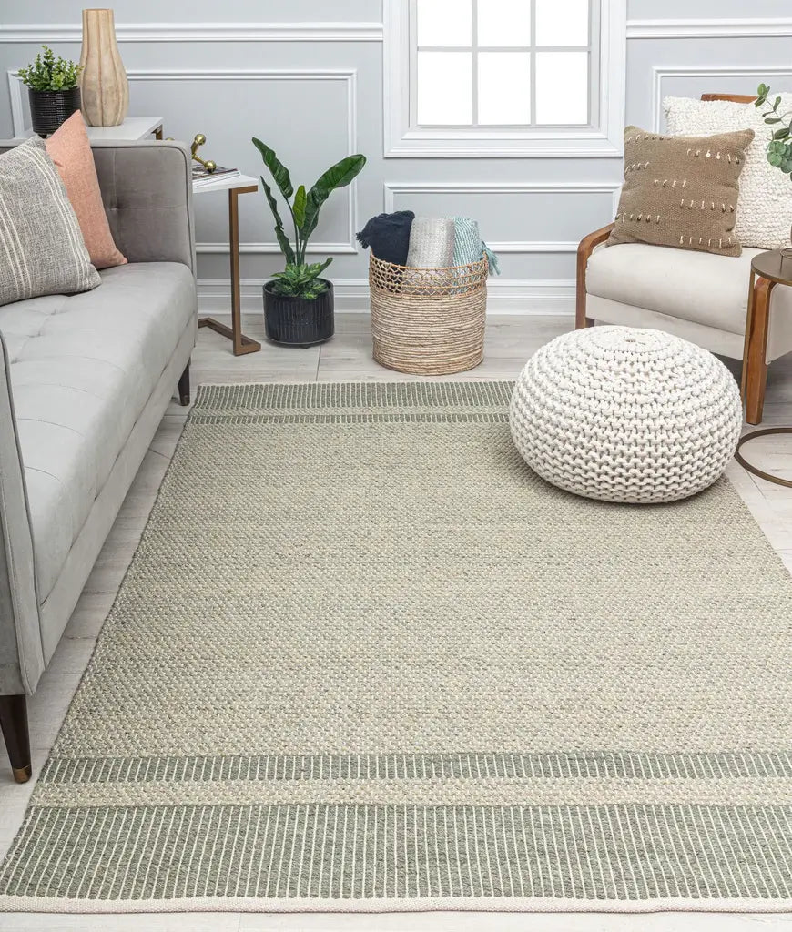 Modern living room with a gray sofa, striped beige rug, wooden armchair, knitted pouf, potted plant, and woven basket