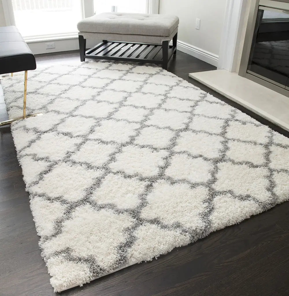 Modern ivory and gray quatrefoil patterned rug in a bright living room, paired with a white bench and dark wood flooring