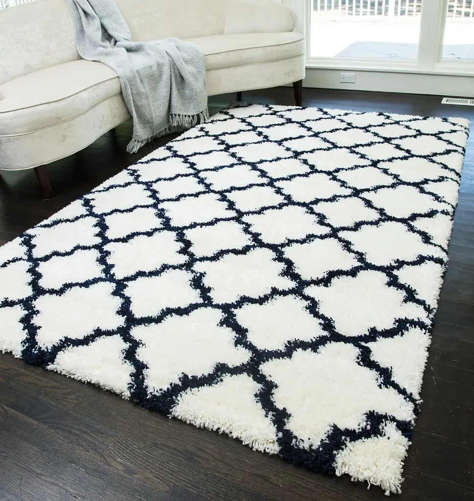 Elegant ivory and navy quatrefoil patterned rug in a stylish living room, featuring a cream sofa with a gray throw, and dark wood floors.