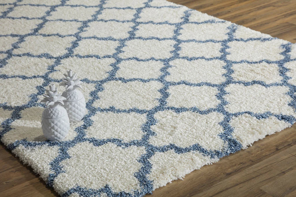 Elegant ivory and light blue quatrefoil patterned rug in a bright room with wooden floors, featuring decorative white pineapples