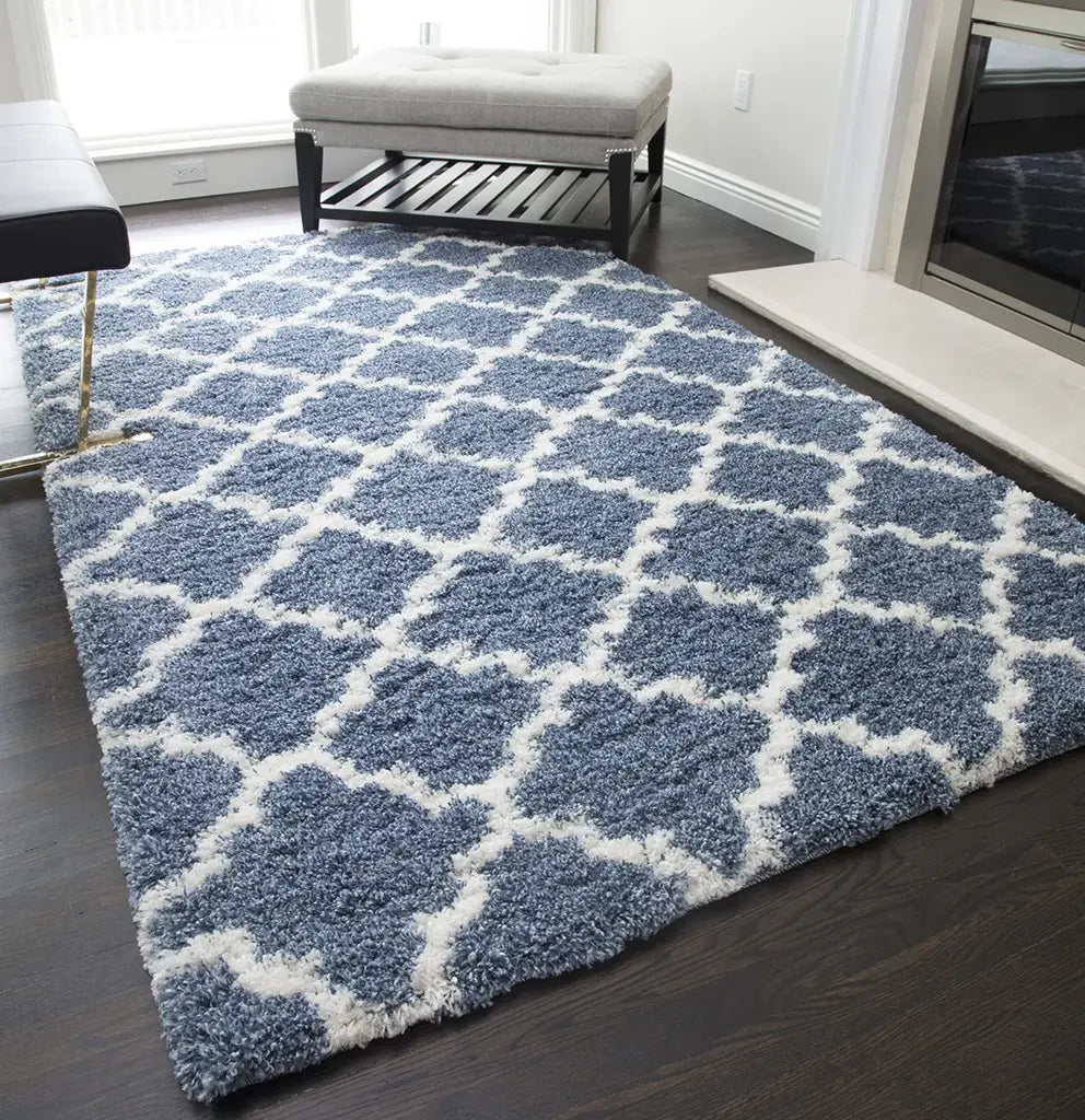 Elegant light blue and ivory quatrefoil patterned rug in a modern living room, complemented by a white bench and dark hardwood flooring