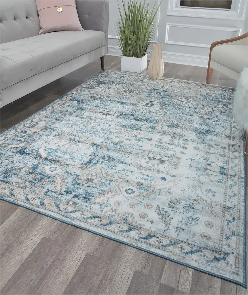 Chic living room with a gray sofa, patterned blue and white rug, wooden floor, green plant, and decorative wooden vases