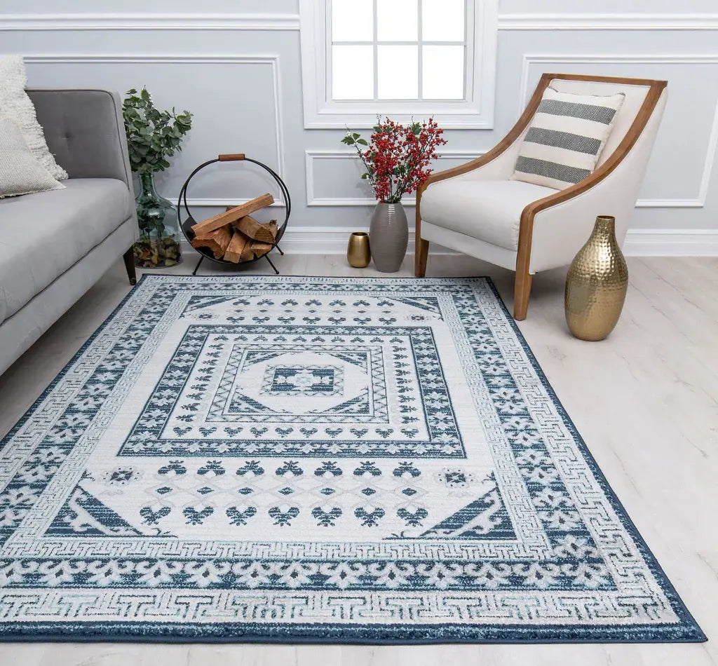 Elegant living room with a grey sofa, a white armchair, a blue and white patterned rug, a rustic firewood holder, and decorative plants