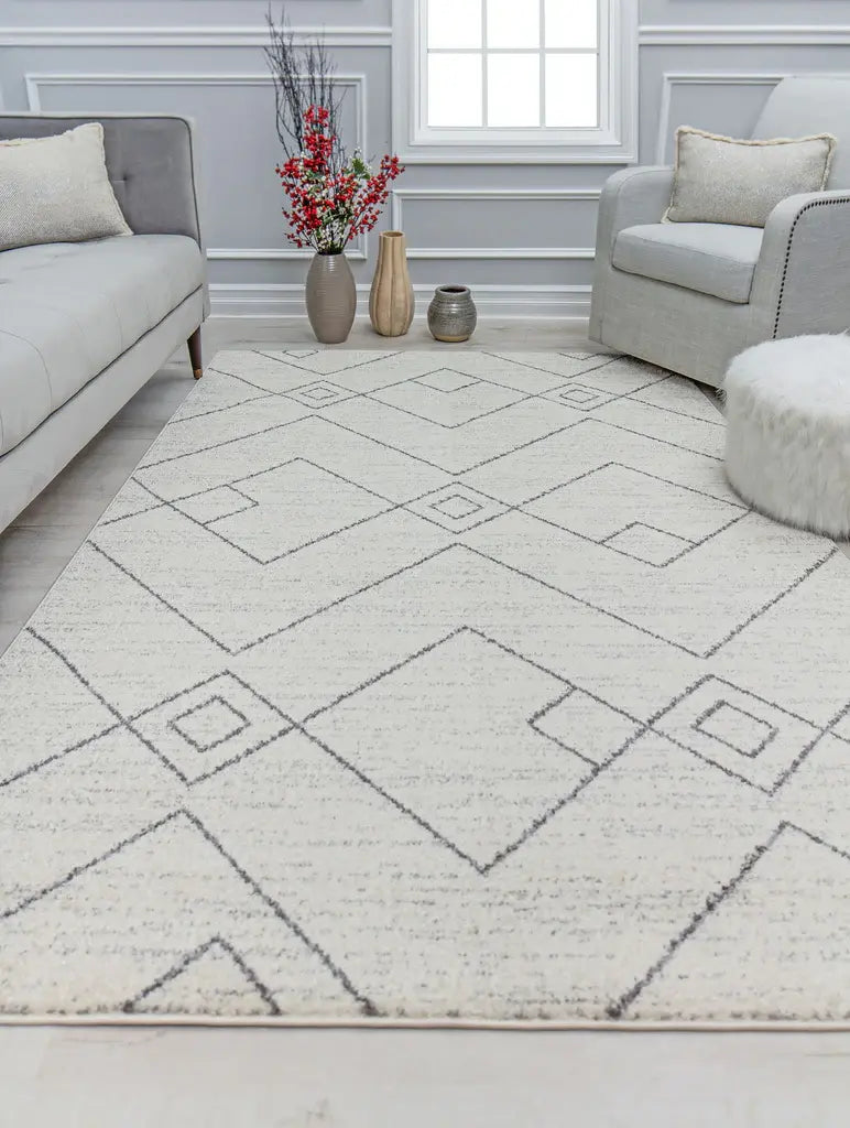 Living room with a gray sofa, beige and pink pillows, white side table, green plant, and a patterned blue and beige area rug on wooden floor.