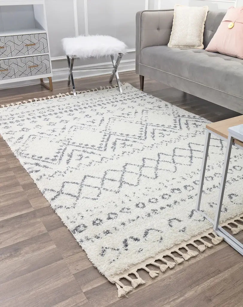 White textured rug with gray geometric patterns in a modern living room featuring a gray sofa, fur stool, and side table.