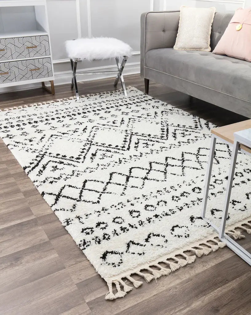 Elegant ivory and black patterned rug with fringes in a modern living room, featuring a gray sofa, decorative pillows, and wood flooring