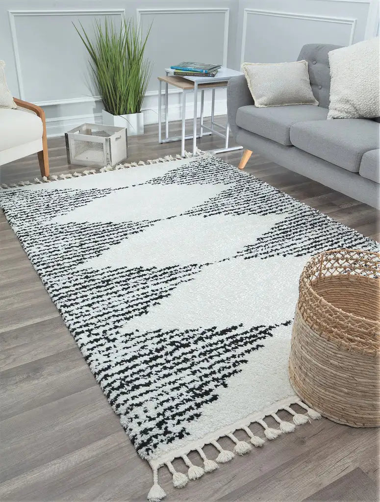 Modern ivory and black patterned rug with fringes in a stylish living room, featuring a gray sofa, decorative pillows, and wood flooring