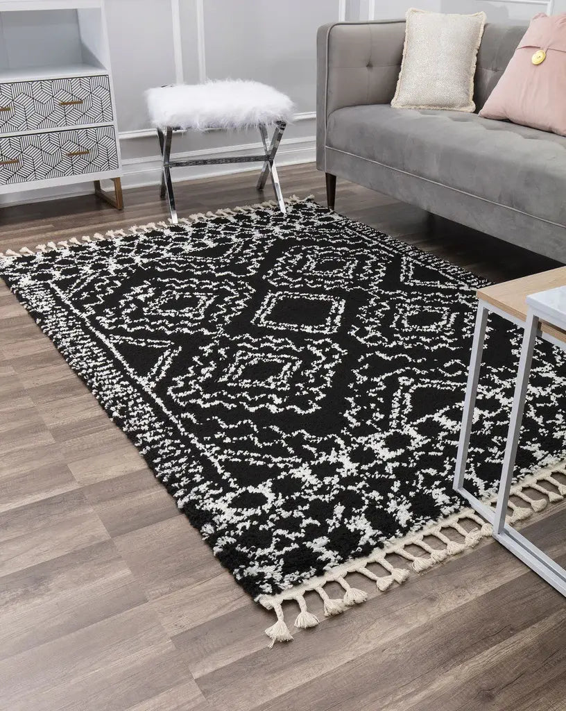 Stylish black and white patterned rug with fringes in a modern living room, featuring a gray sofa, decorative pillows, and wood flooring