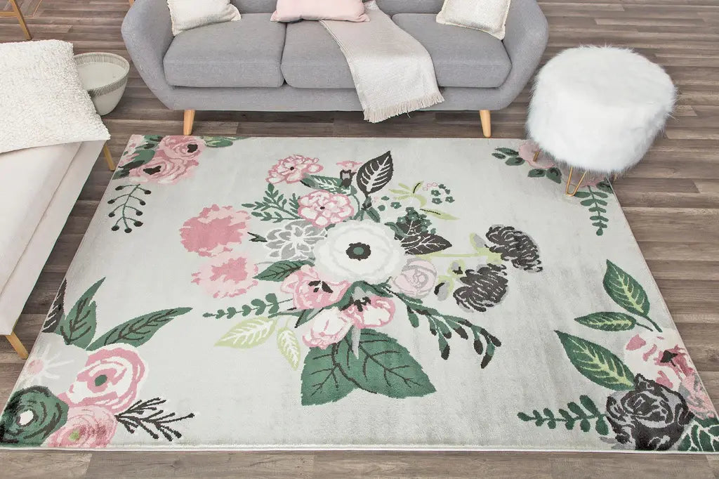 Living room featuring a floral area rug with pink and green accents, complementing the grey couch and white fluffy ottoman.